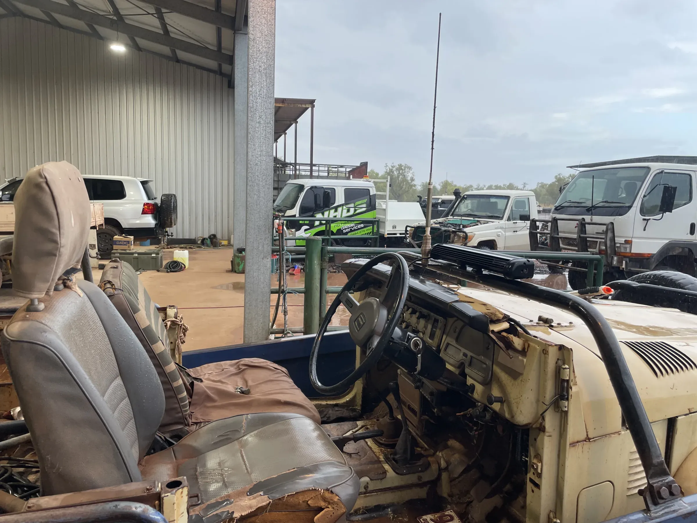 Old Toyota stripped back for repairs in a station shed, with the NHDS service truck and other vehicles behind