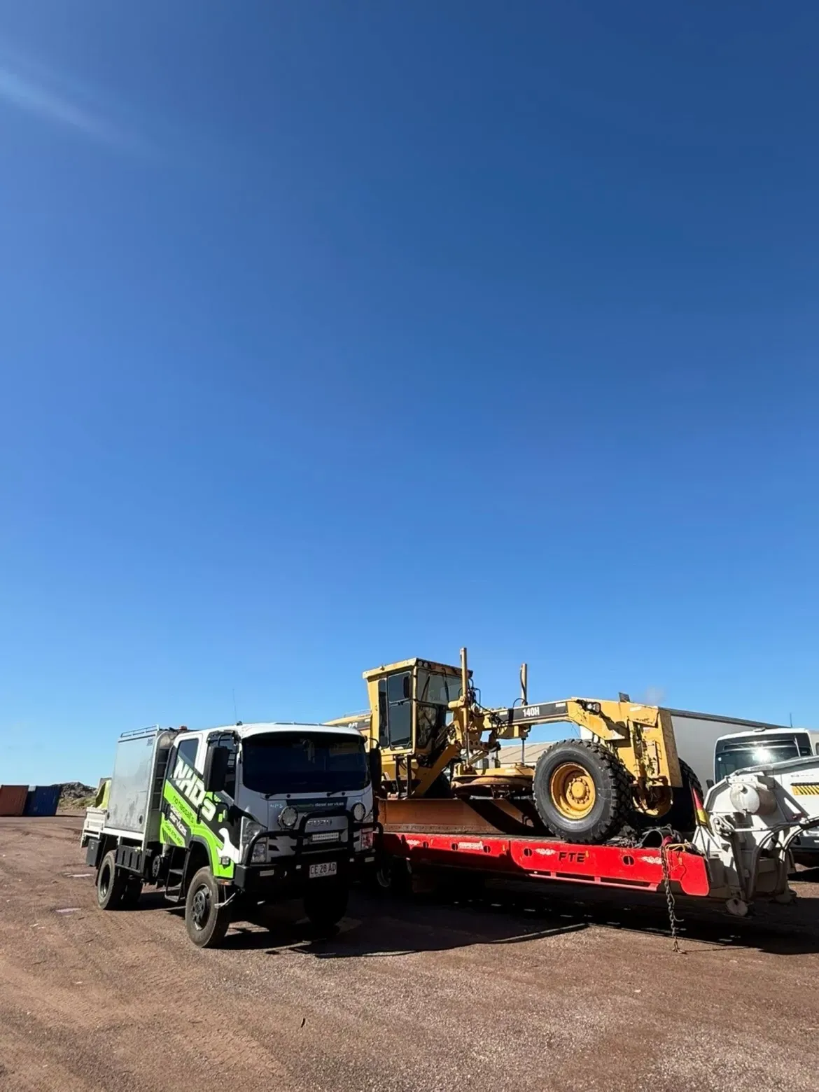 NHDS service truck beside a grader loaded on a float, ready to head out